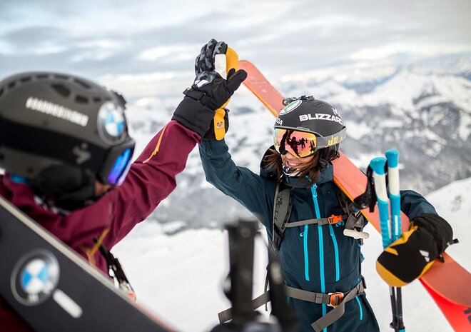 Two skiers in winter gear celebrate their successes on a snow-covered mountain with skis and ski goggles.