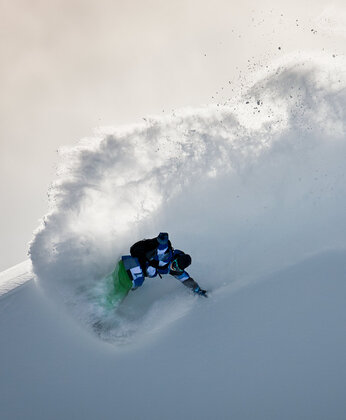 Ein Snowboarder fährt durch tiefen Pulverschnee auf einer hellen, verschneiten Piste.