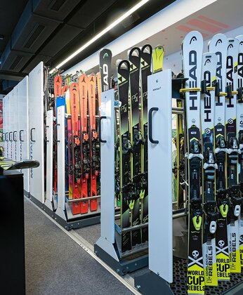 Several rows of different skis are neatly arranged on racks in a shop.