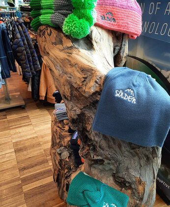 Colorful knitted hats with pom-poms and the Sölden logo on a wooden stand in a shop.