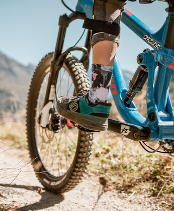 Nahaufnahme einer Person, die ein blaues Mountainbike auf einem felsigen Weg in einer bergigen Umgebung fährt.