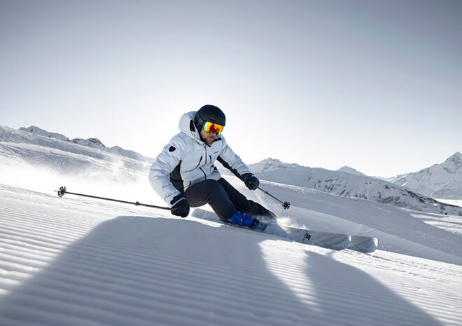 Ein Skifahrer in Winterausrüstung fährt an einem sonnigen Tag in einer verschneiten Berglandschaft durch frischen Schnee.