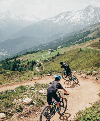 Zwei Radfahrer fahren mit ihren Mountainbikes auf einem Trail dem berg hinab