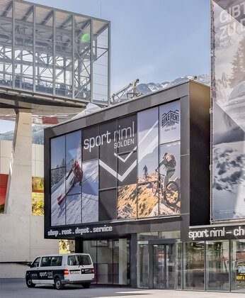 Eine Glasfront mit einer große Werbetafel und einem geparkten Auto vor dem Geschäft
