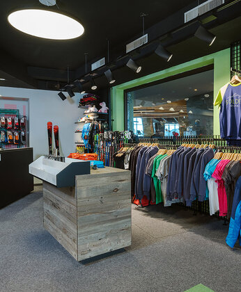 Ein Bekleidungsgeschäft mit Regalen mit bunten Bekleidung, einem hölzernen Tresen und einem großen Schaufenster, in dem sich das Geschäft spiegelt.