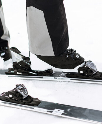 Nahaufnahme der Füße einer Person, die Skier und schwarz-weiße Skischuhe auf dem Schnee trägt.