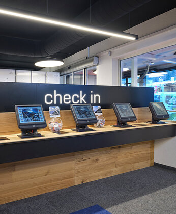 A row of self-service check-in kiosks under a “Check-in” sign in a modern, brightly lit room.