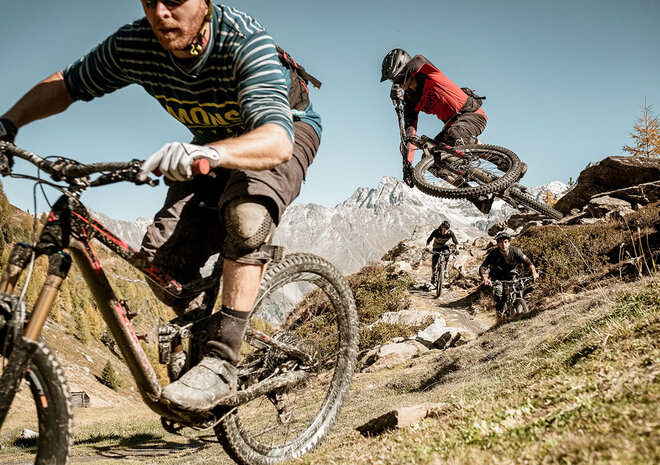 Zwei Mountainbiker fahren an einem sonnigen Tag mit ihren Bikes einen felsigen Weg in einer malerischen, bergigen Landschaft hinunter.